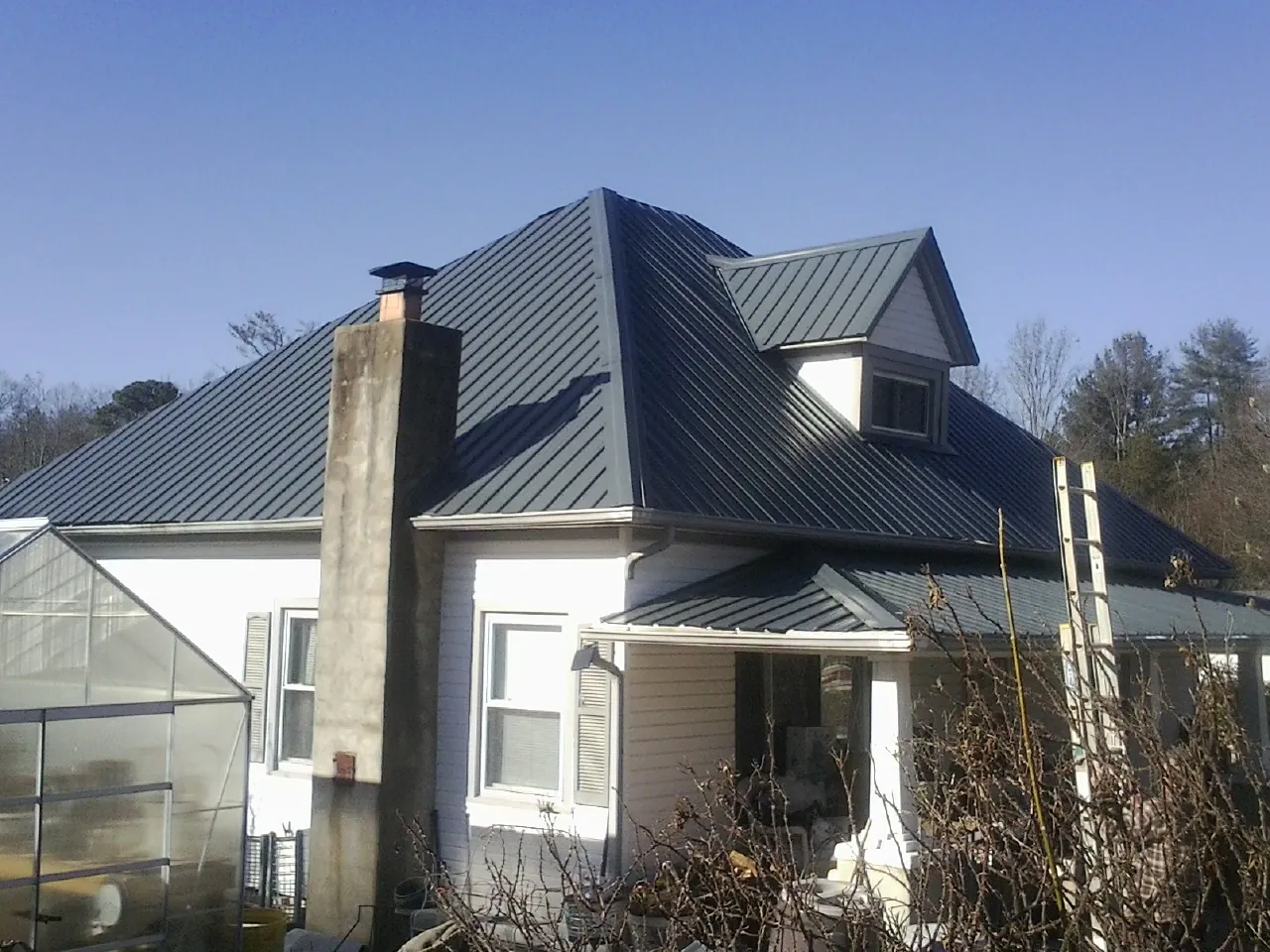 Dark blue standing seam metal roof on a white farmhouse with dormer — Slate & Tile Roof Repair by Roofing Brothers in Mannsville