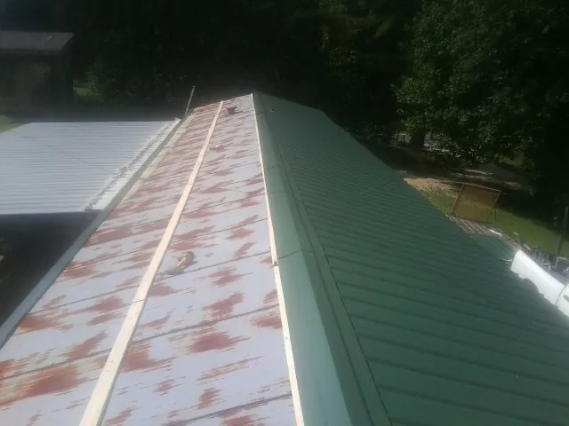 Old rusted panels beside newly installed green metal roofing — Wind Damage Roof Repair by Roofing Brothers in Mannsville