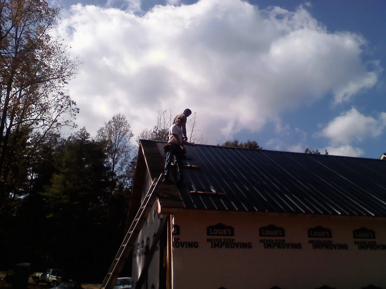 Roofer fastening dark metal panels high against a cloudy sky, from a Roof Inspection job in Mannsville