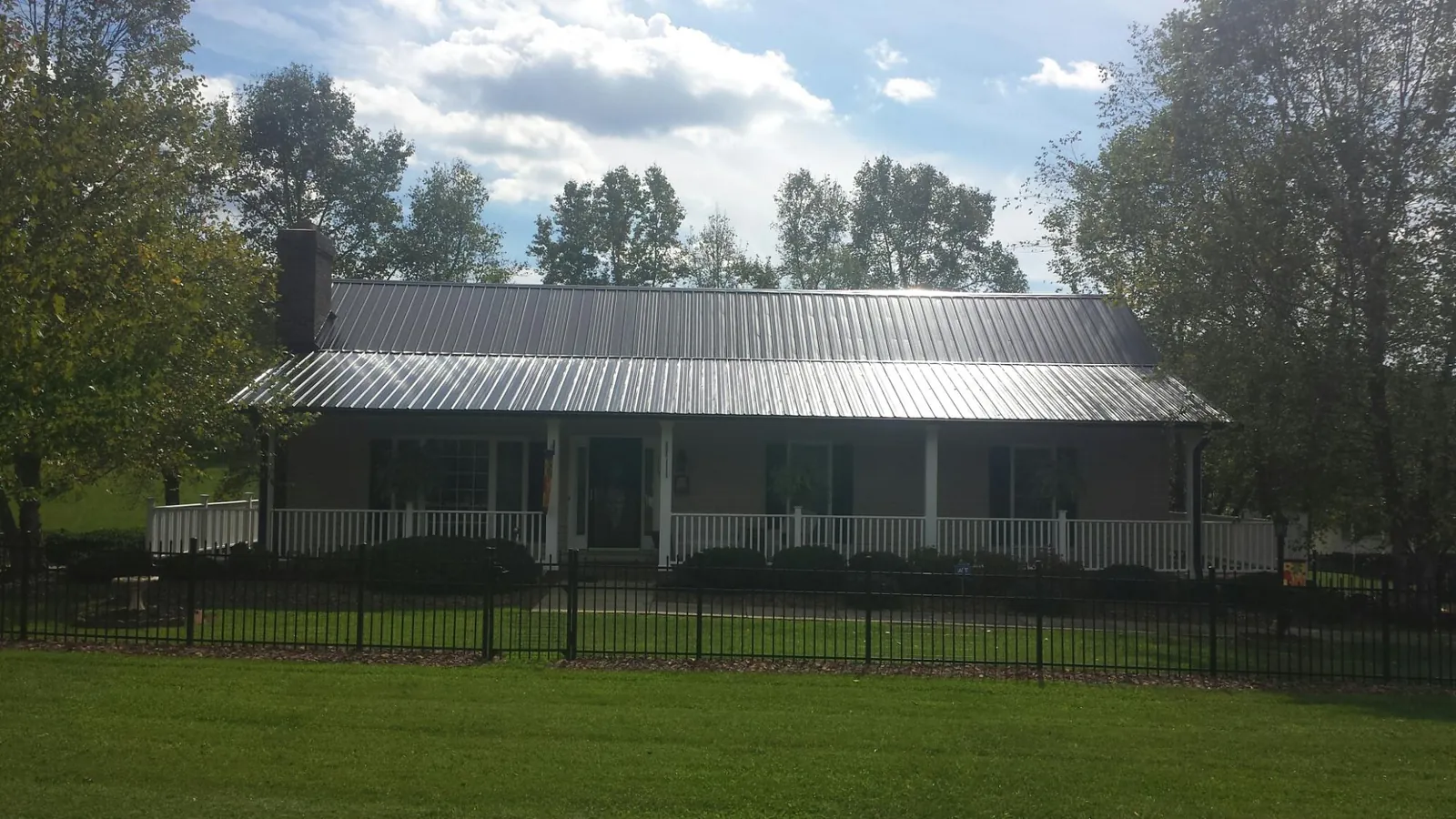 Gray metal roof on a brick ranch with a full width front porch — Gutter Guard Installation work by our crew in Mannsville